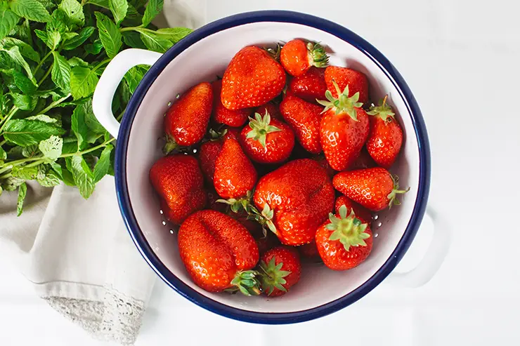 Bowl blanco con fresas apoyado sobre una mesa blanca. Al lado del bowl hay unas hojas de menta