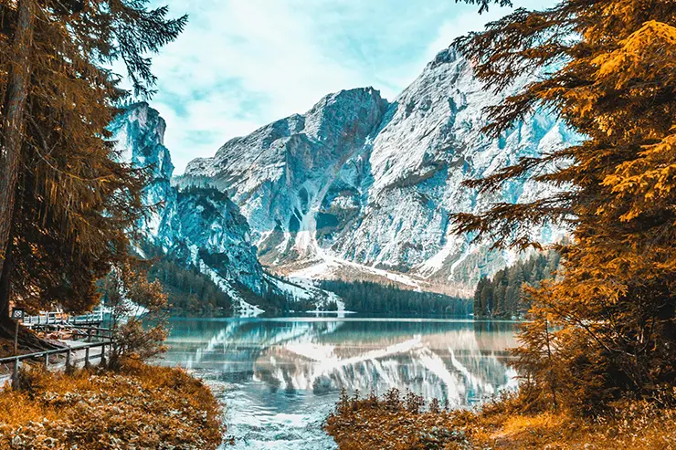 Montañas nevadas en el fondo, debajo un lago cristalino y alrededor árboles con hojas amarillas tradicionales del otoño
