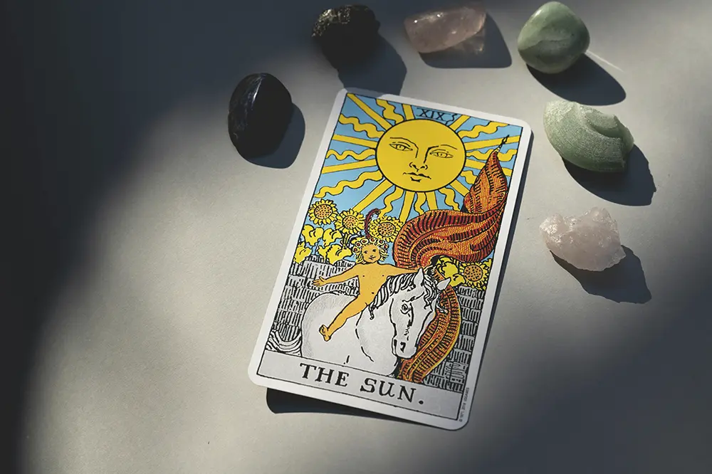 Carta de Tarot "El Sol" apoyada sobre una mesa, alrededor unas piedras de colores