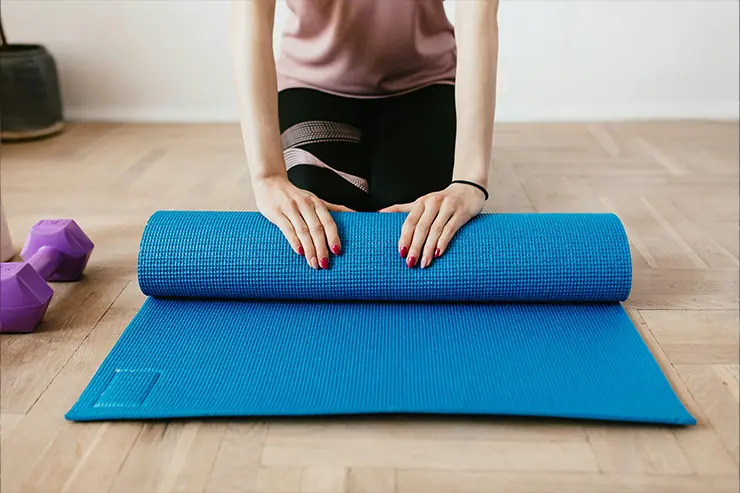 Torso de mujer, sentada sobre sus rodillas enrollando una estirilla de yoga.