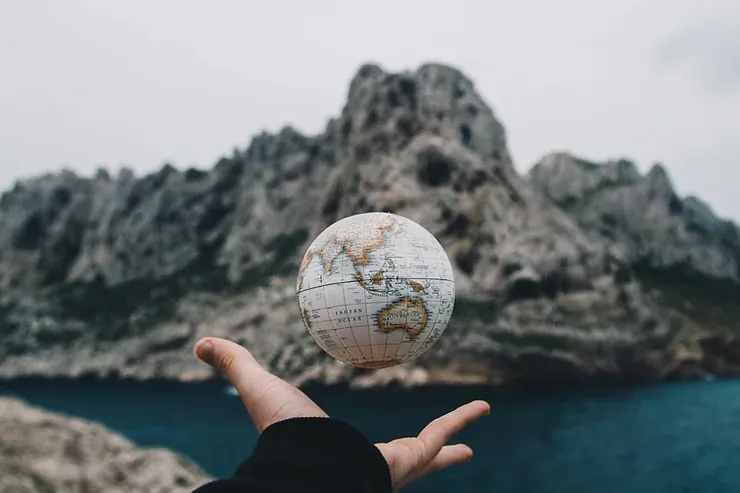 Mano abierta de una persona sosteniendo un globo terráqueo, con un fondo de lagos y montañas.