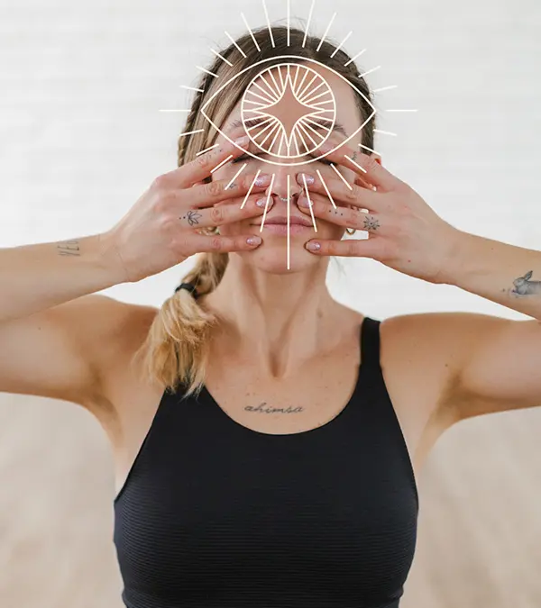 Una mujer blanca de 28 años, de piel clara y cabello rubio recogido en una coleta, con un top deportivo negro, cubriéndose los ojos con las manos, con tatuajes en los brazos y el pecho, y un dibujo de un ojo blanco superpuesto sobre su rostro.